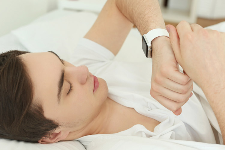 Young man with sleep tracker lying in bed